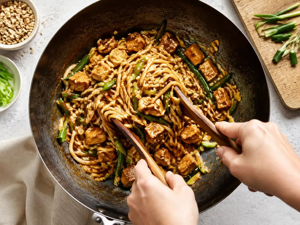 Erdnuss-Nudeln und Tofu werden im Wok vermengt